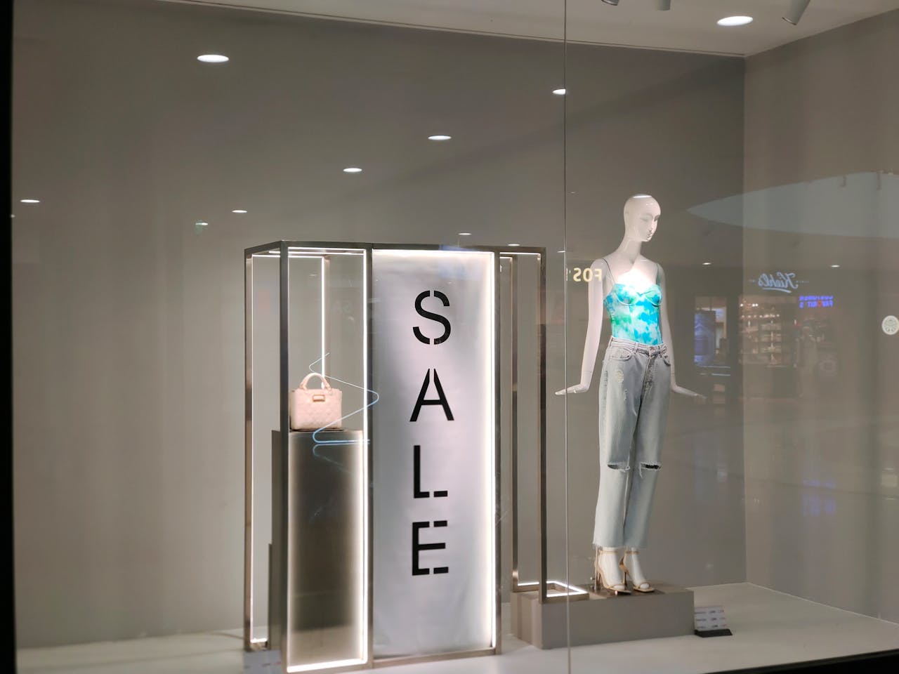 Stylish window display featuring sale sign and fashionable mannequin in trendy outfit.